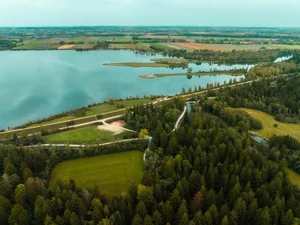 Entdecken Sie Königsbrunn! Luftaufnahme eines Sees mit angrenzendem Wald und Feldern auf dem Land