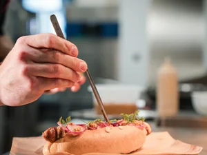 Cervus: das Restaurant in Königsbrunn mit dem gewissen Extra Hand, die mit Pinzette Zutaten auf einem Hotdog arrangiert