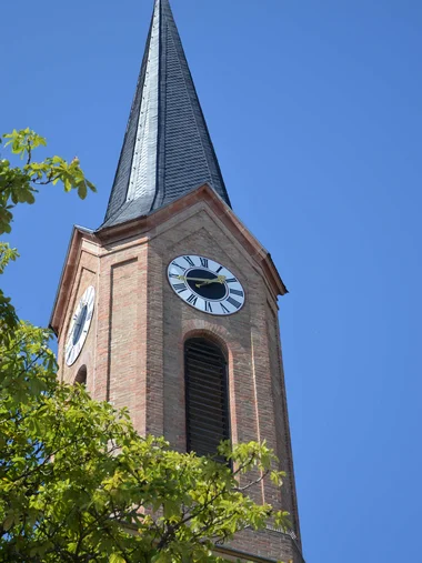 Entdecken Sie Königsbrunn! Kirchturm mit Ziffernblatt und spitzem Dach vor klarem blauem Himmel