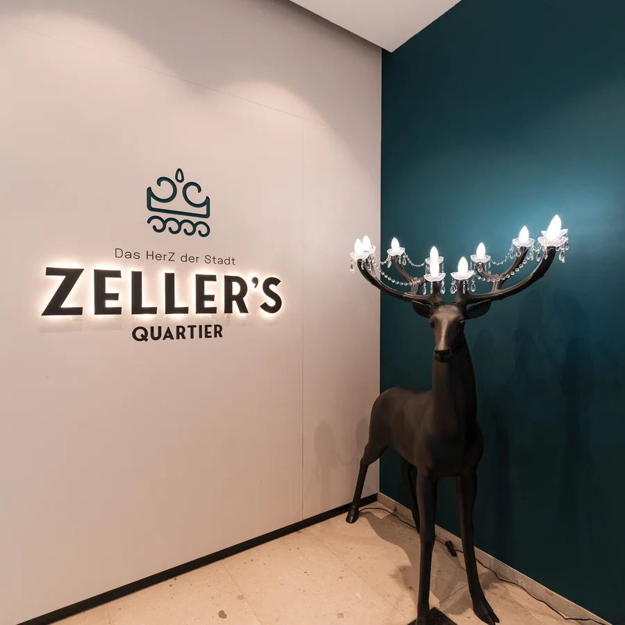 Cervus: Ihre Eventlocation in Augsburg und Umgebung Eingangsbereich mit leuchtendem Zeller's Quartier Logo und schwarzem Rentier-Lampenständer
