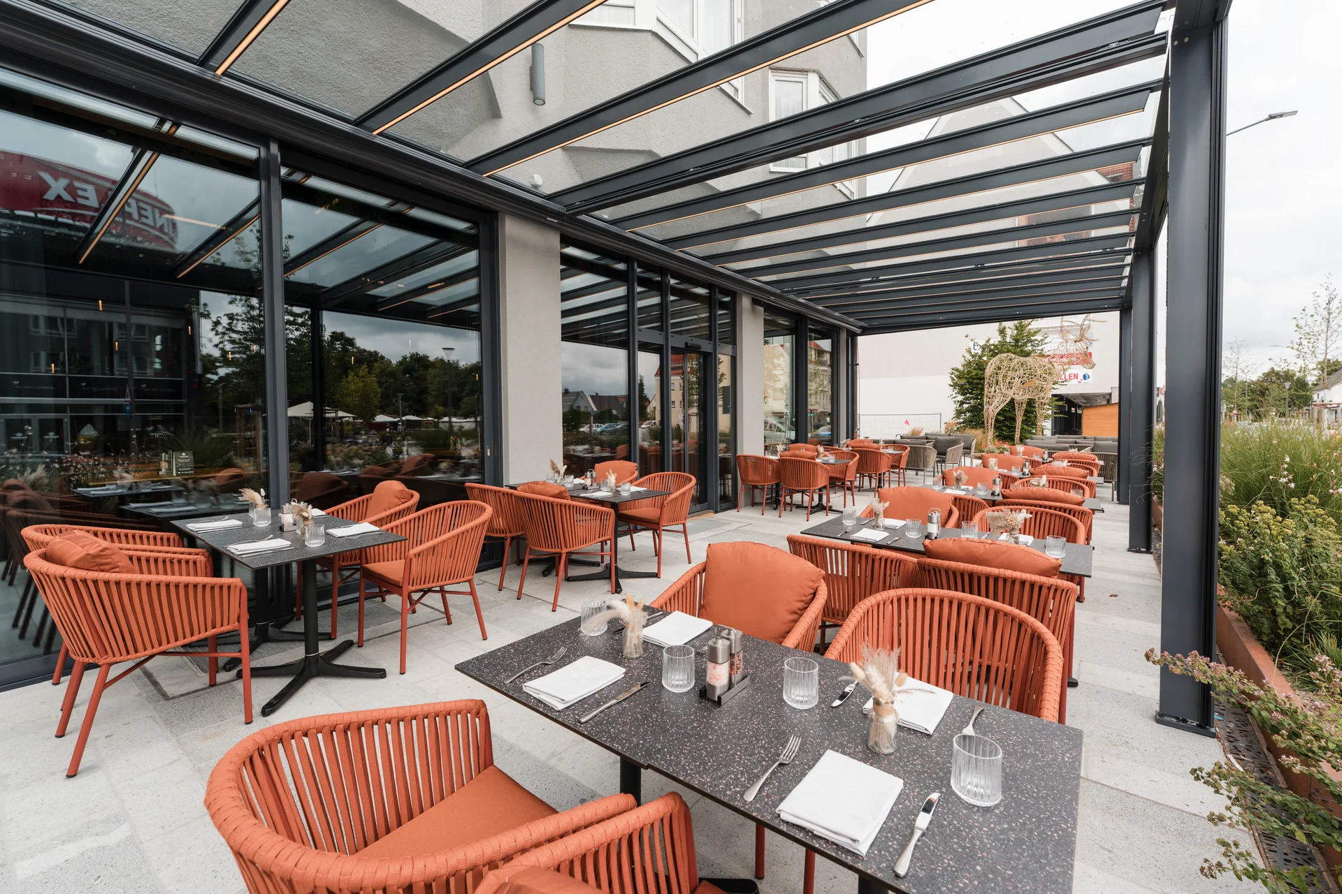 Cervus: das Restaurant in Königsbrunn mit dem gewissen Extra Außenbereich eines Restaurants mit roten Stühlen und eingedeckten Tischen unter Glasdach
