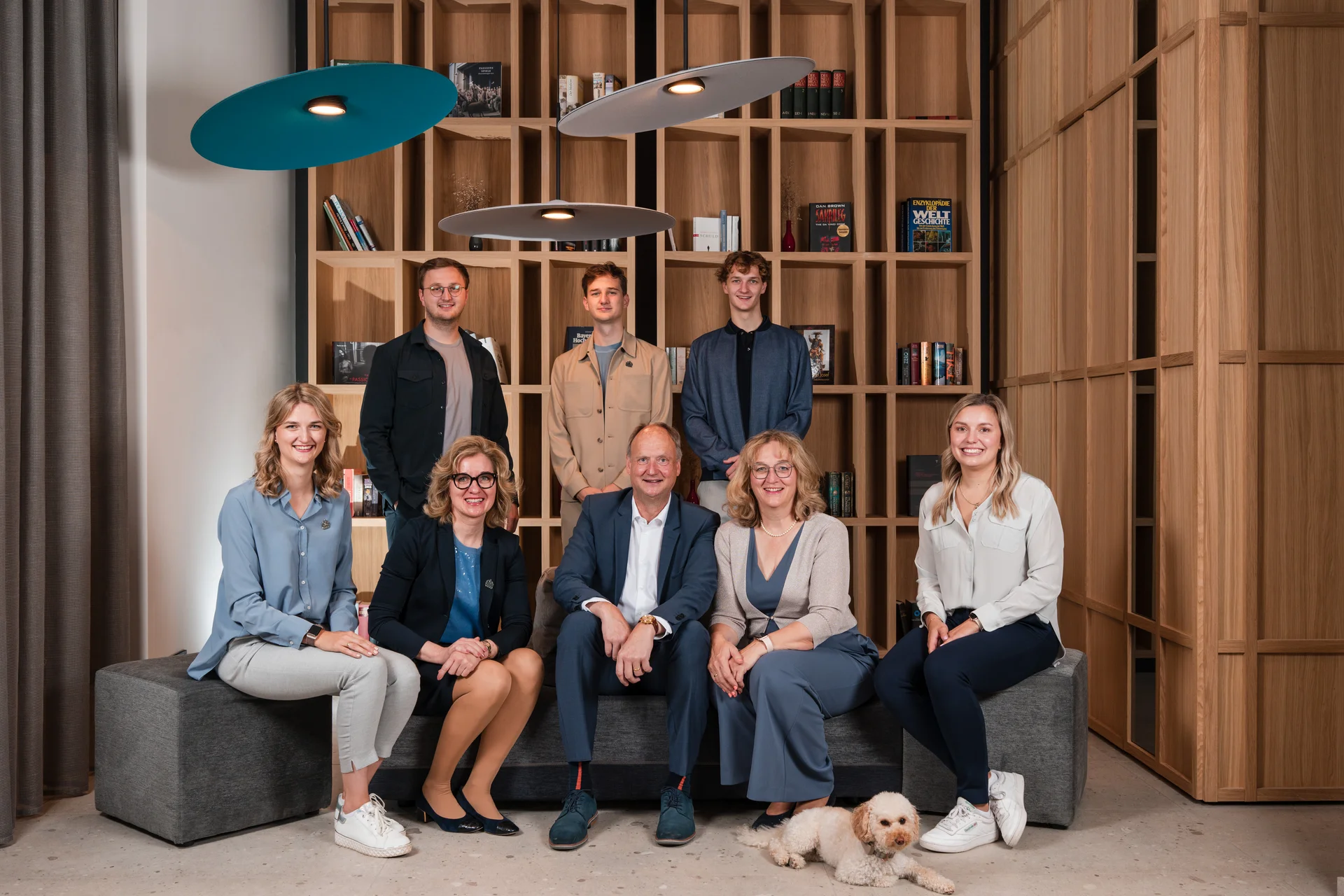 Ihre Gastgeber in Zeller’s Quartier Gruppenbild von acht Menschen und einem kleinen Hund in einem modernen Raum mit Bücherregal