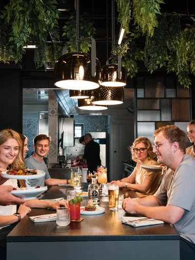 Cervus: Ihre Eventlocation in Augsburg und Umgebung Gäste genießen Essen in modernem Restaurant mit servierenden Kellnern und Hängeregalen