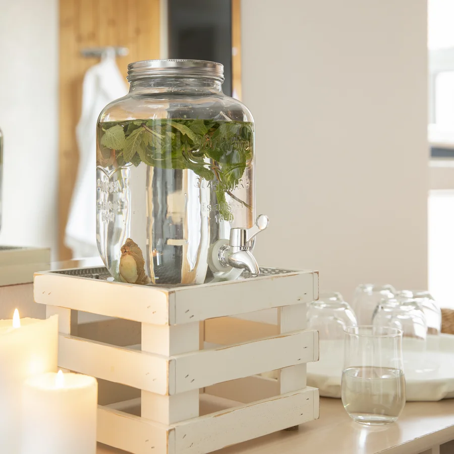 Ihr besonderes Hotel in Königsbrunn: Zeller’s Quartier Wasserspender mit Kräutern auf Holzgestell neben brennenden Kerzen und Gläsern