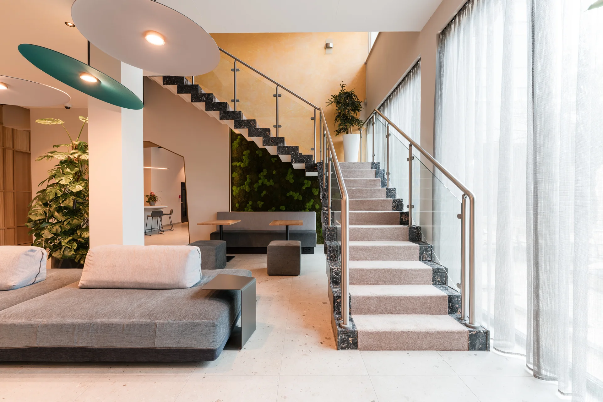 Ihr besonderes Hotel in Königsbrunn: Zeller’s Quartier Moderner Wohnbereich mit grauer Couch und Treppe mit Teppich und Glasgeländer