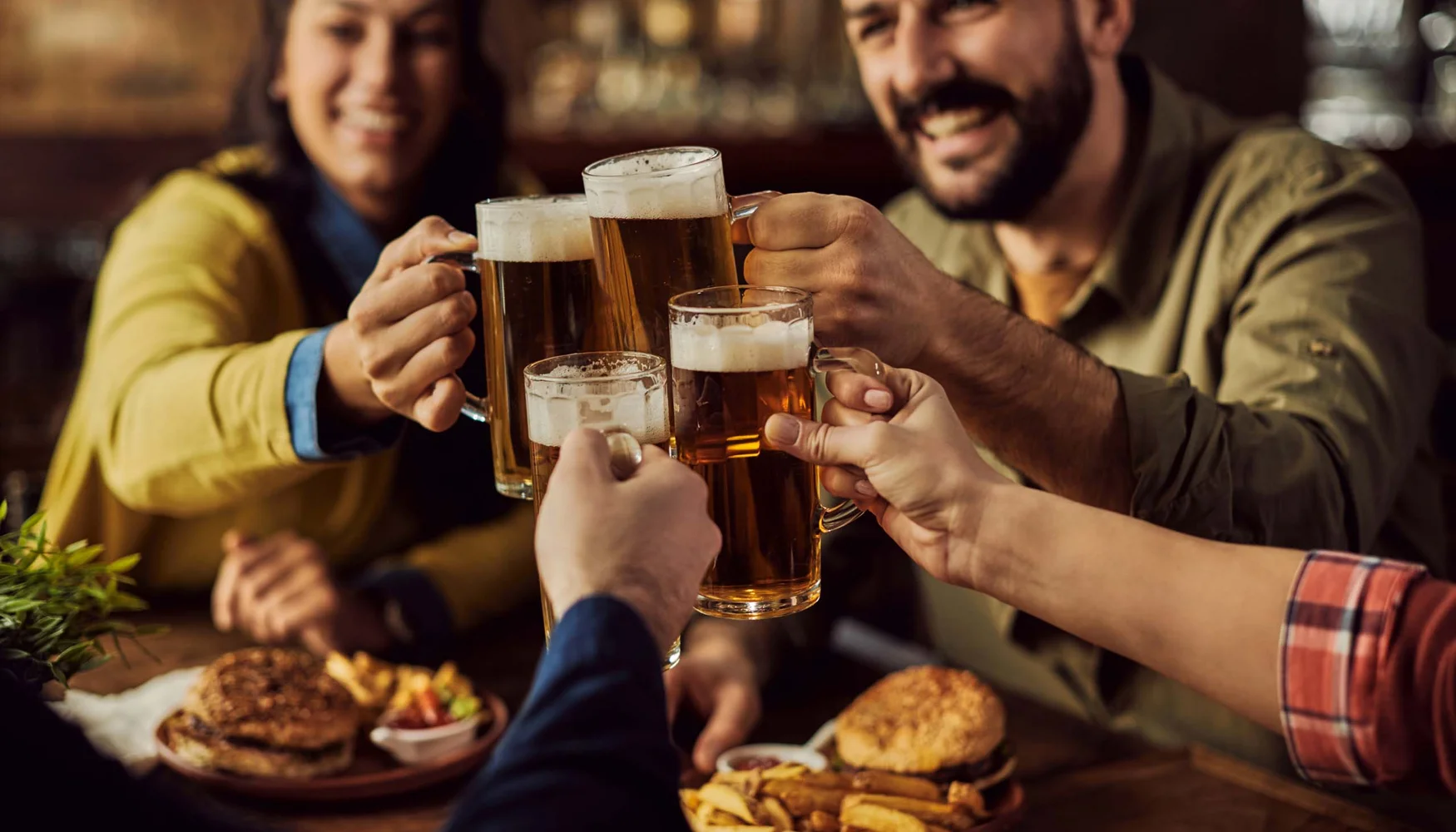 Biergarten rund um Königsbrunn gesucht? Freunde stoßen mit Biergläsern an in einem Restaurant mit Burgern und Pommes