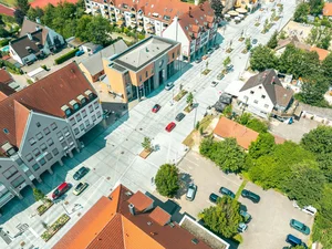 Entdecken Sie Königsbrunn! Luftaufnahme einer Straße mit Gebäuden, Autos und Bäumen an einem sonnigen Tag