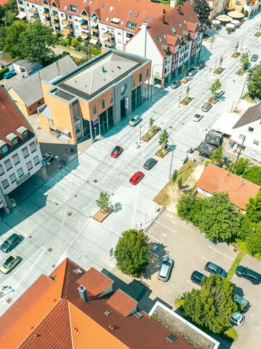 Zeller’s Quartier – das HerZ der Stadt Königsbrunn Luftaufnahme einer Straße mit Gebäuden, Autos und Bäumen an einem sonnigen Tag