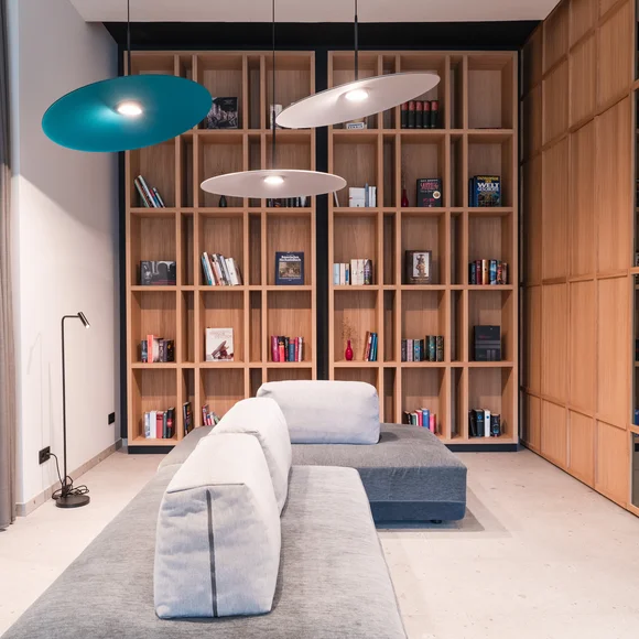 Ihr besonderes Hotel in Königsbrunn: Zeller’s Quartier Moderner Wohnbereich mit grauem Sofa, Holzbücherregal und hängenden Lampen
