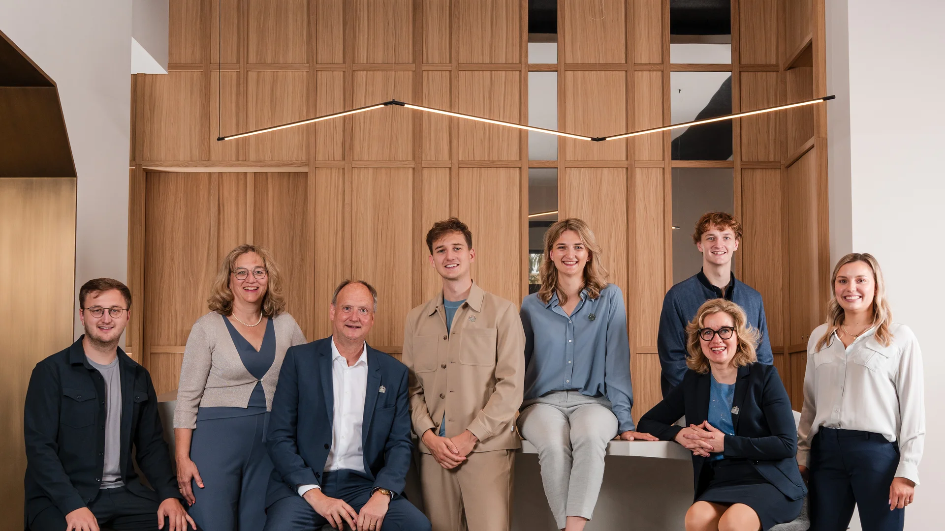 Ihre Gastgeber in Zeller’s Quartier Gruppenfoto von acht Personen vor einer Holzpaneelwand in modernem Büro