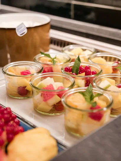 Ihr Start in den Tag: Frühstück in Königsbrunn Gläser mit frischem Obstsalat, garniert mit Minzblättern auf weißem Teller
