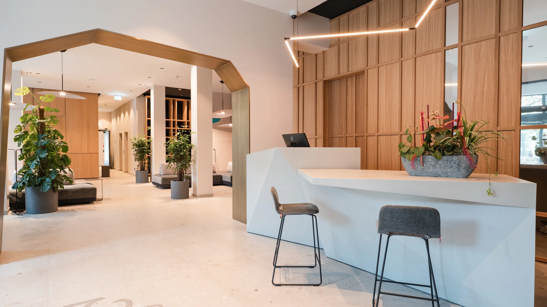 Ihr besonderes Hotel in Königsbrunn: Zeller’s Quartier Moderner Empfangsbereich mit weißer Theke, zwei Hockern und Pflanzen