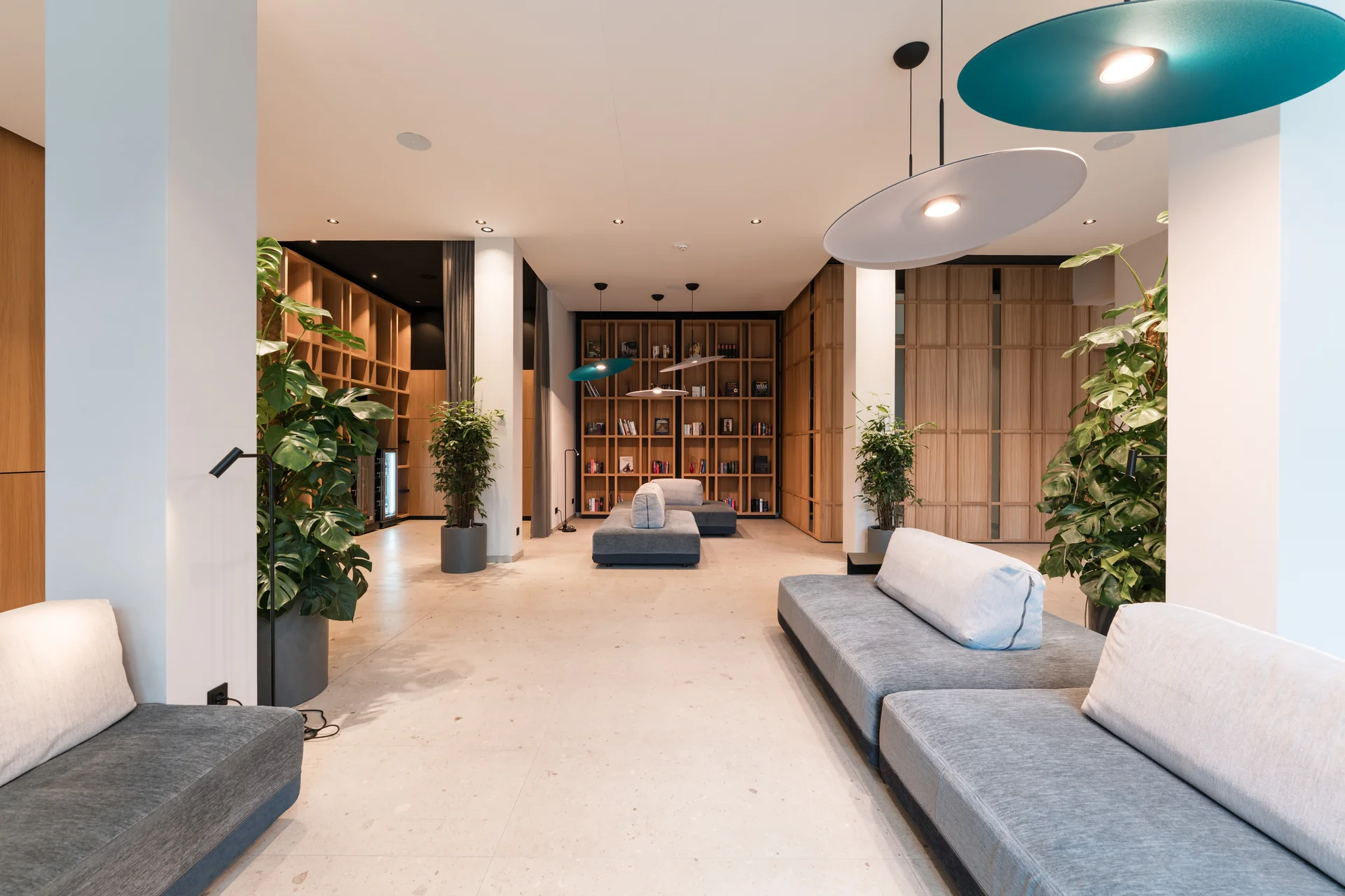 Zeller’s Quartier – das HerZ der Stadt Königsbrunn Moderner Wartebereich mit grauen Sofas, hölzernen Regalen und grünen Pflanzen