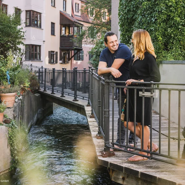 Ihr besonderes Hotel in Königsbrunn: Zeller’s Quartier Zwei Personen unterhalten sich auf einer Brücke am Wasser in Augsburg.