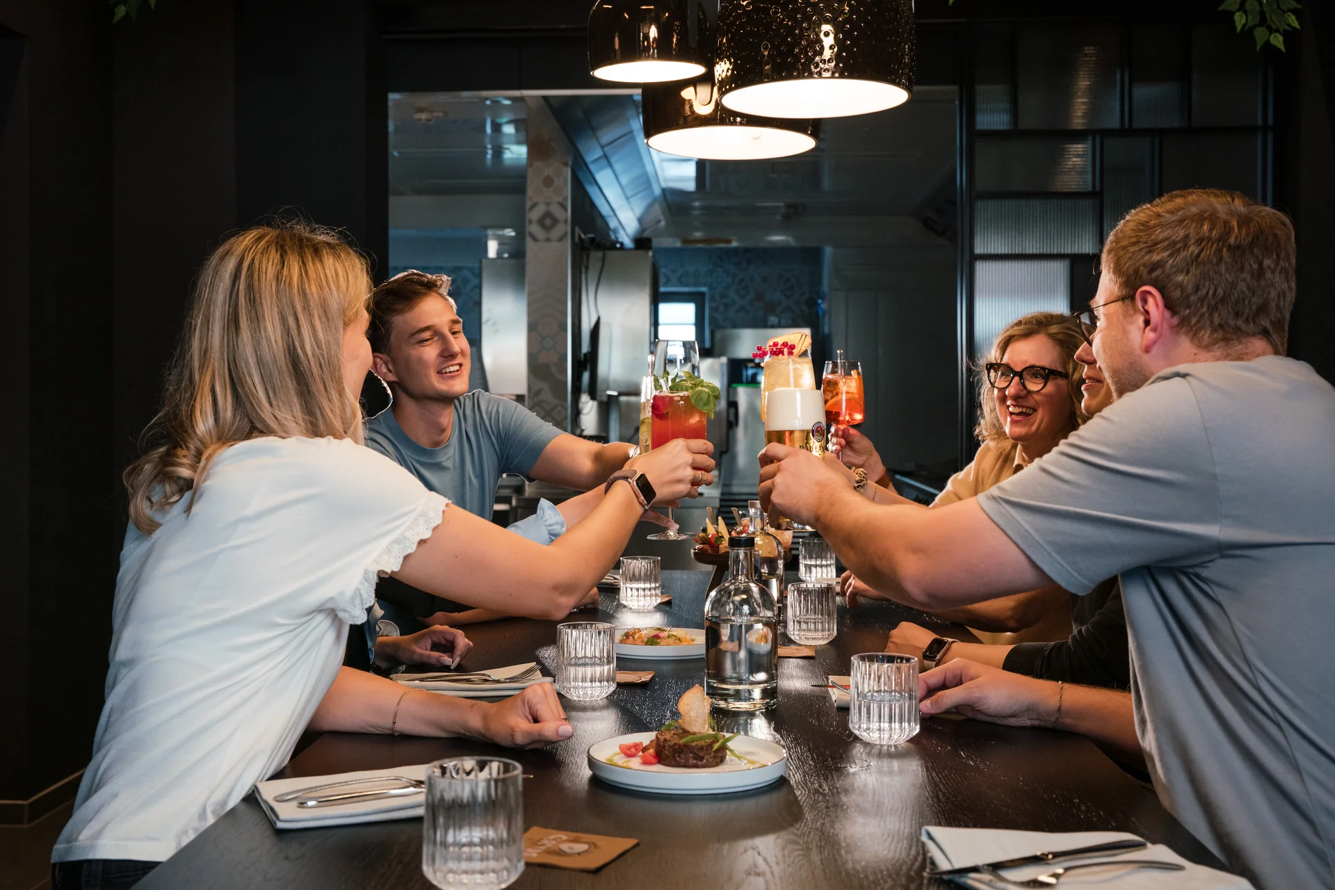 Ihr besonderes Hotel in Königsbrunn: Zeller’s Quartier Gruppe von Freunden stößt mit Getränken an am Esstisch in modernem Restaurant