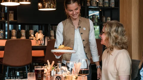 Zeller’s Quartier und Cervus in Königsbrunn: Stellenangebote Kellnerin serviert einem Gast in einem Restaurant ein Gericht mit Lächeln