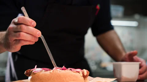 Zeller’s Quartier und Cervus in Königsbrunn: Stellenangebote Koch dekoriert Gourmet-Hotdog mit Zange in professioneller Küche