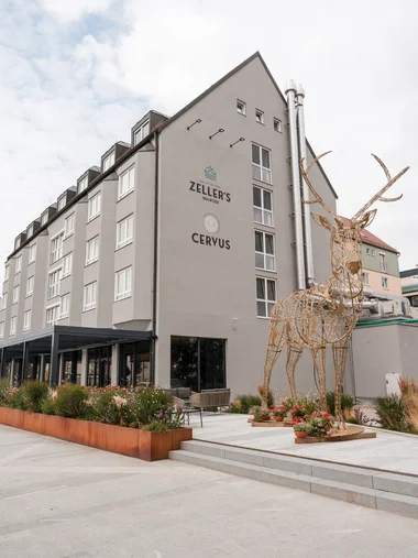 Ihre Gastgeber in Zeller’s Quartier Moderne Gebäude mit Metallskulptur eines Hirsches und bepflanztem Vorgarten