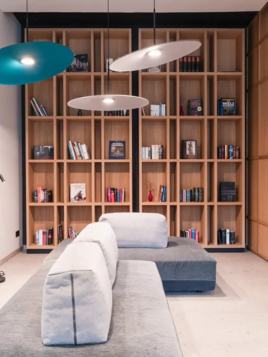 Ihr besonderes Hotel in Königsbrunn: Zeller’s Quartier Moderner Wohnbereich mit grauem Sofa, Holzbücherregal und hängenden Lampen