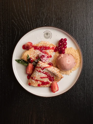 Speisekarten Ein dekorierter Crêpe mit Erdbeeren und einer Kugel Eis auf einem weißen Teller