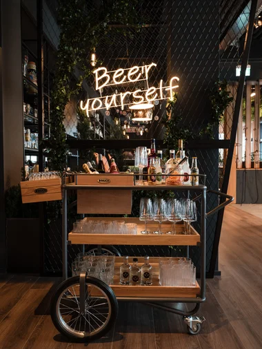 Cervus: das Restaurant in Königsbrunn mit dem gewissen Extra Getränkewagen mit Gläsern und Flaschen vor einem Neonzeichen Beer yourself